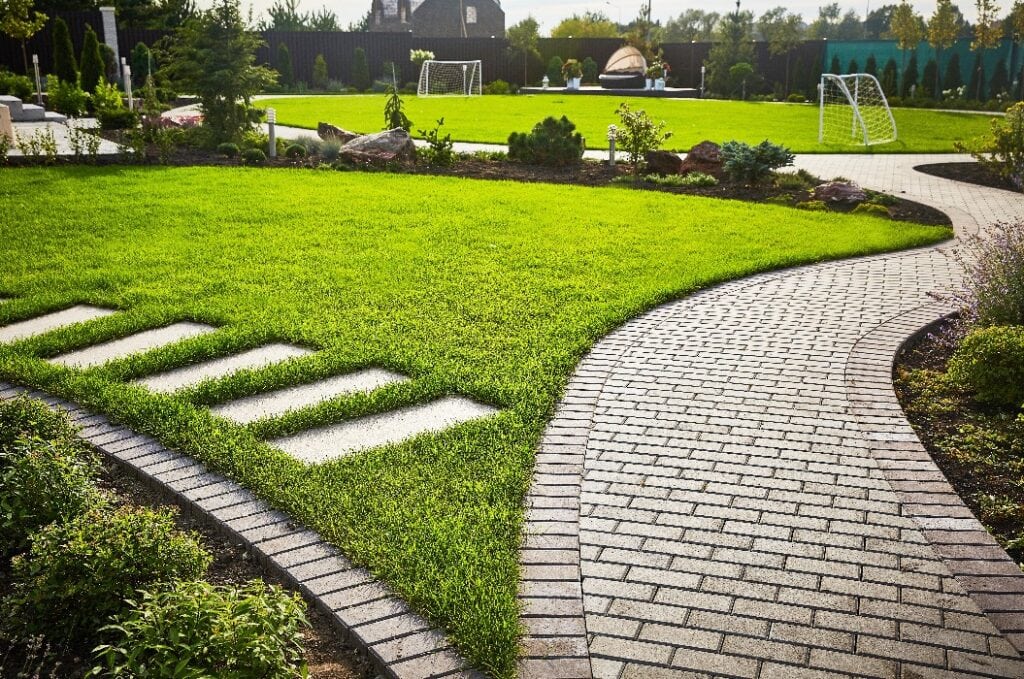 Landscaping of the garden. path curving through Lawn with green grass and walkway tiles.